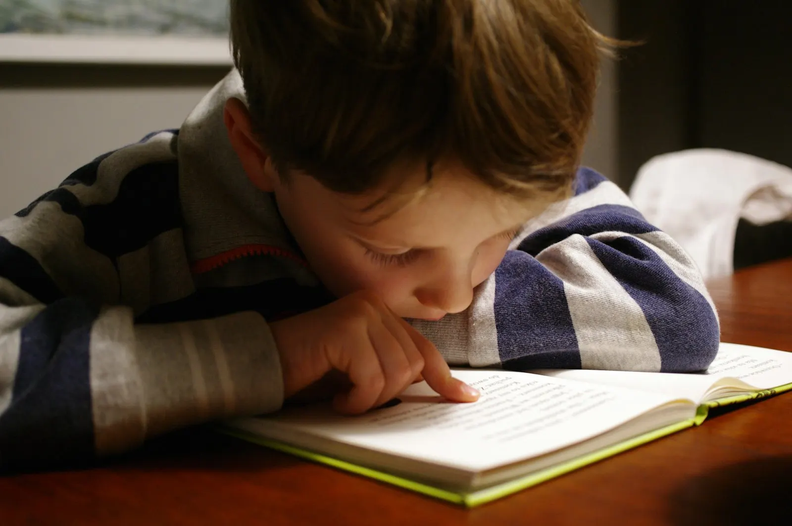 A young boy reading a book, following the words with his finger