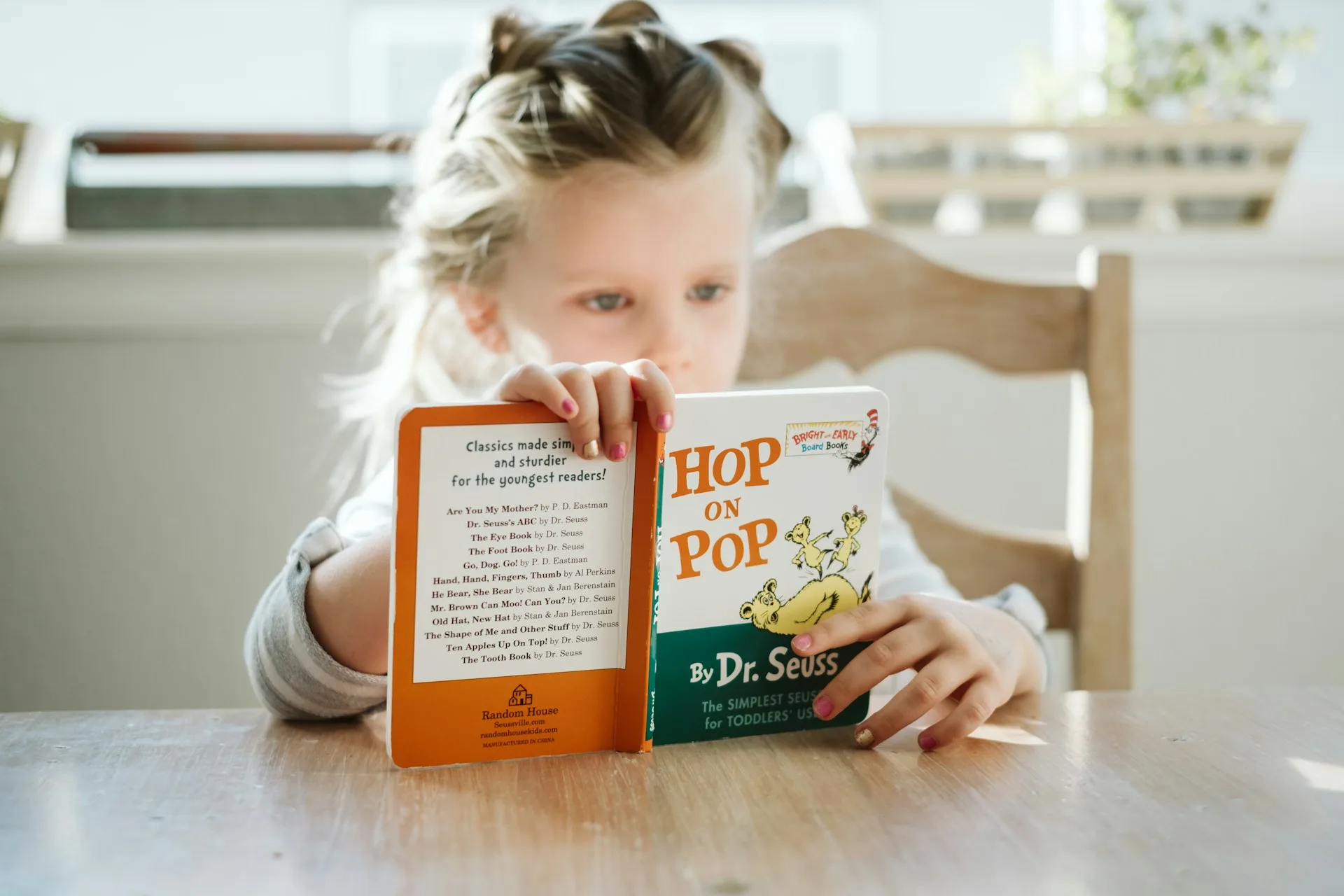 A young girl reading the book Hop on Pop by Dr. Seuss at a kitchen table
